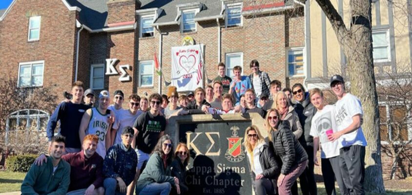 Brothers gathered around chapter house sign on annual Mom’s Day event.